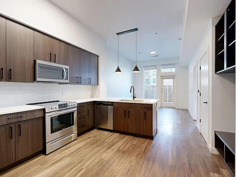 Apartment Kitchen with Stainless Steel Appliances, Dining and Living Room with Plank Flooring and Balcony.