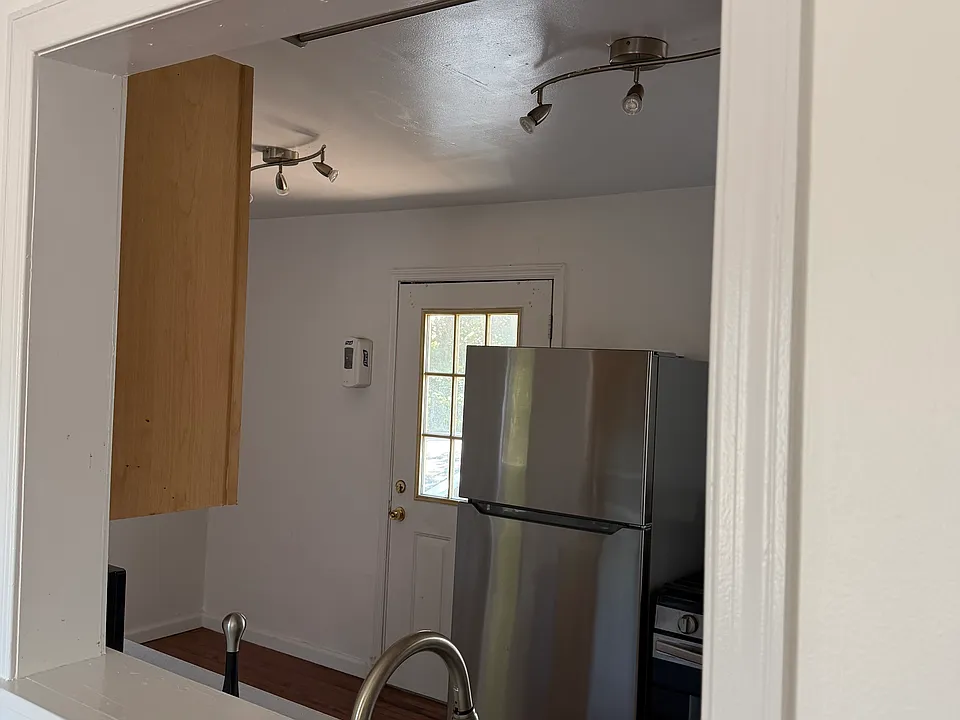 view of kitchen from living room wall cut out showing stainless steel fridge and door to deck