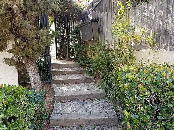 Private gated entrance to condo complex leading to grass area and fruit trees. Unit has a front patio area.