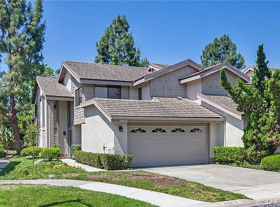 Elevation of this beautiful end unit with trees and sidewalk to the gated and fenced interior grounds and ponds.