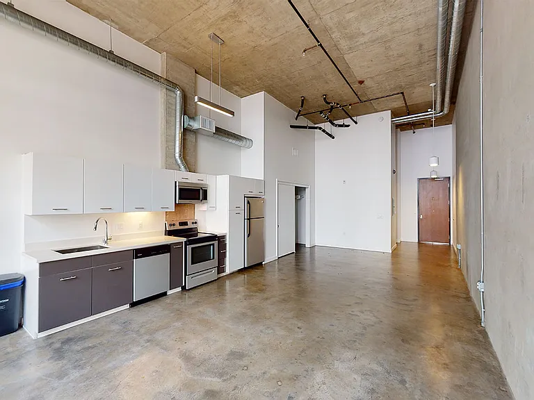 Apartment kitchen with stainless steel appliances, dining and living room with polished concrete flooring.