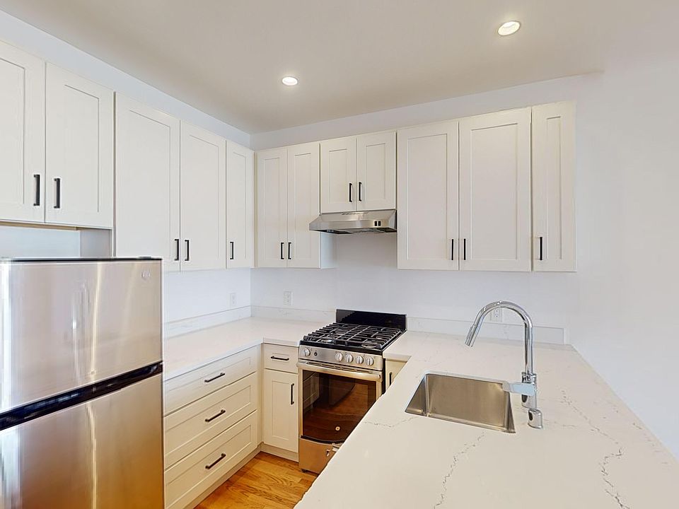 Kitchen with multiple cabinets, refrigerator, stove, range hood, and sink