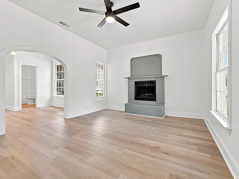 Spacious living area featuring wood-finish flooring, a contemporary ceiling fan, and a fireplace with a gray brick surround