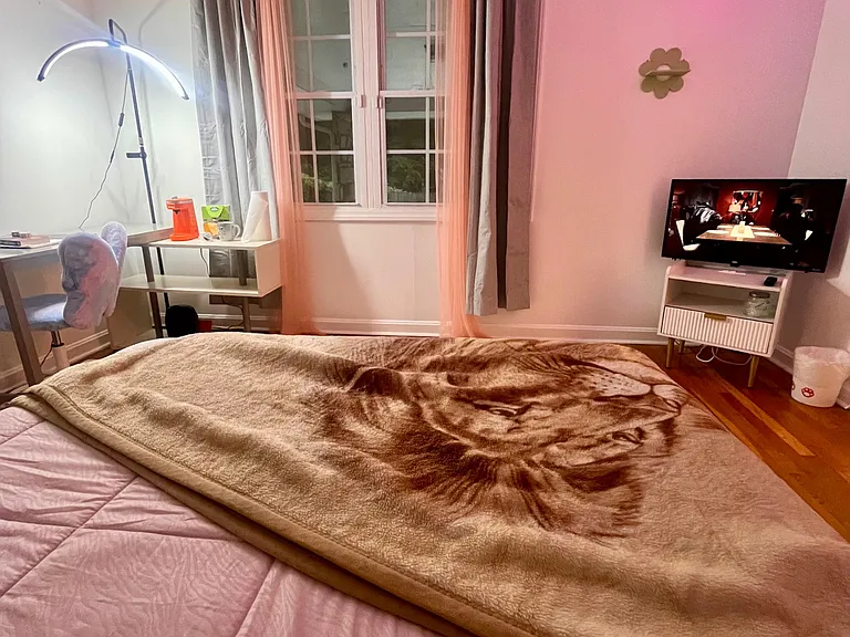 Bedroom with a large window and layered curtains, plus space for a desk setup and a TV stand for easy downtime.