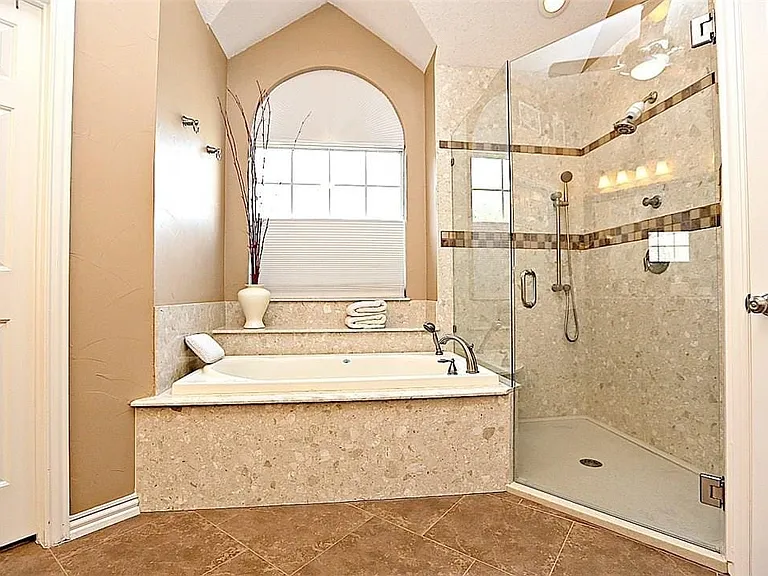 Alcove bathtub with an arched window, featuring a glass-enclosed shower with tiled walls and a handheld showerhead