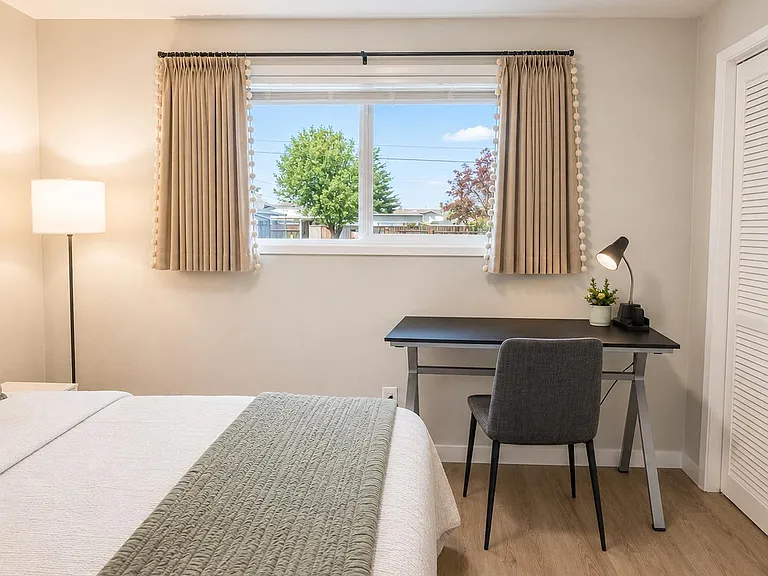 Well-appointed bedroom with a large window, dedicated desk workspace, and a roomy closet with louvered doors.
