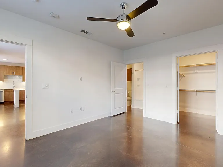 Spacious apartment bedroom with large closet, attached bathroom, and polished concrete flooring.