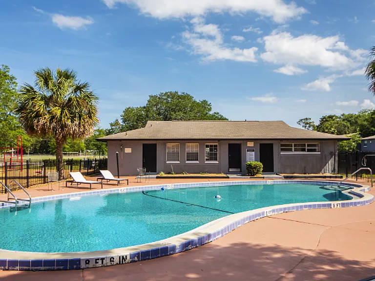 Inviting poolside area featuring a refreshing swimming pool, modern sun loungers, and a cozy clubhouse surrounded by lush greenery in a serene setting.
