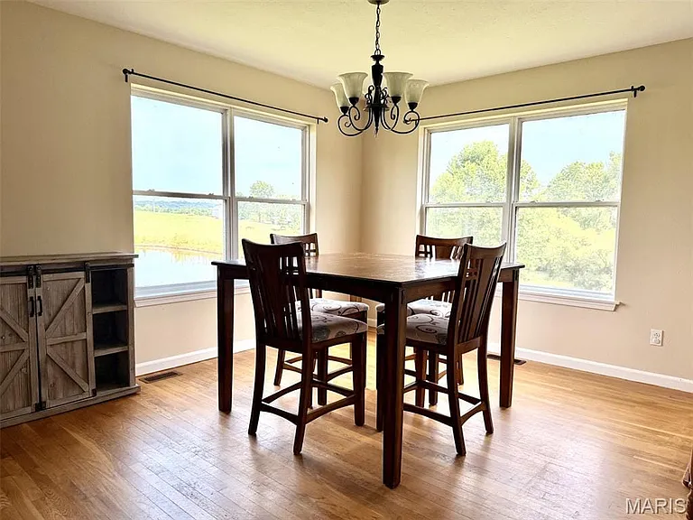 Hardwood flooring, corner windows with trim, and a chandelier with glass shades