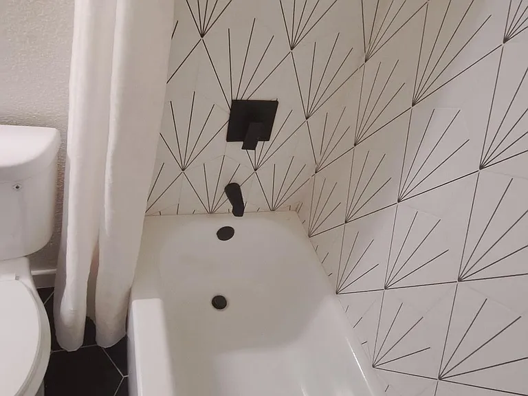 Full bathroom with a tub/shower combo, patterned tile surround, and matte-black fixtures for a clean, updated look.