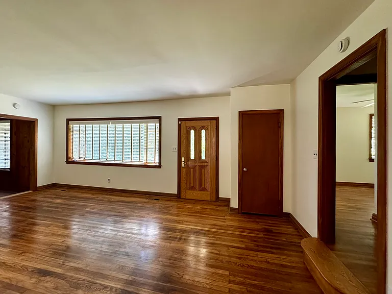 Living room with hardwood flooring; front door, closet; looking into Bedroom 1 (at right).