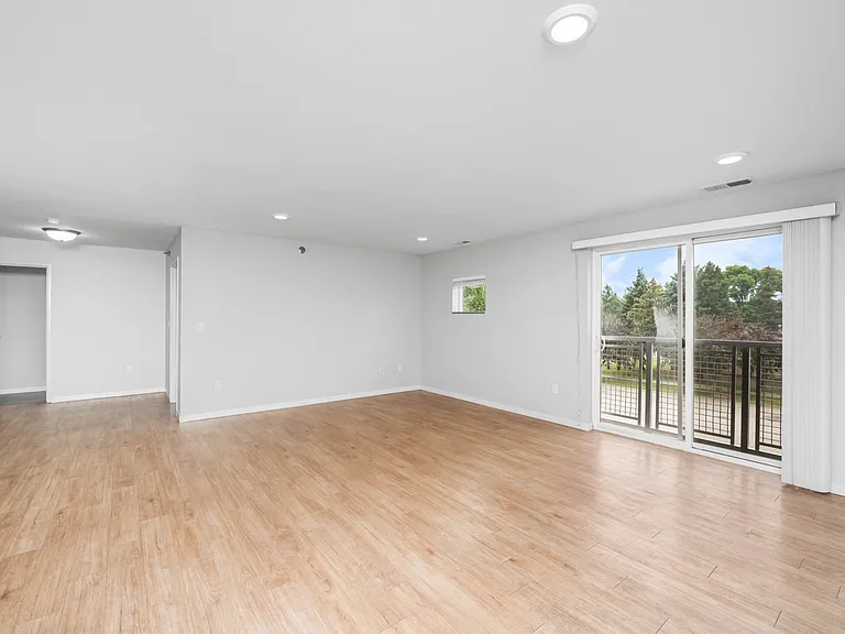 Spacious open-concept living area with elegant wood flooring and bright natural light from large sliding glass doors leading to a balcony with scenic views. Spacious open-concept living area with elegant wood flooring and bright natural light from large s