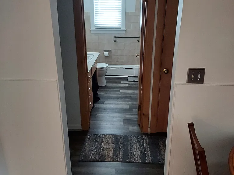 Heading from the living/dining room into the hallway, then into the bathroom w/ new flooring throughout. The master bedroom is down the hall on the left and the second bedroom is down the hall on the right.