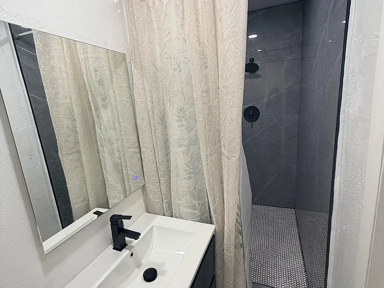 Updated bathroom featuring a sleek vanity, framed mirror, and a walk-in tiled shower with modern black fixtures.