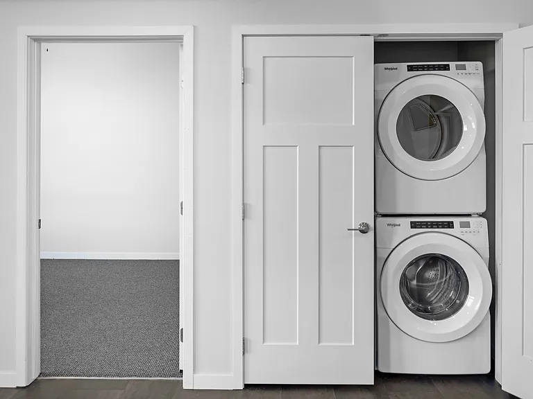 Modern apartment with in-unit stacked washer and dryer next to a cozy carpeted room. Modern apartment with in-unit stacked washer and dryer next to a cozy carpeted room.