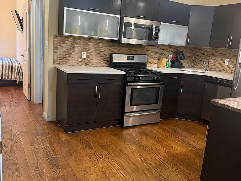Updated kitchen with dark cabinetry, mosaic tile backsplash, and stainless steel range, microwave, and dishwasher.