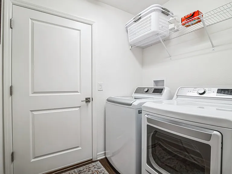 Laundry Room with a Smart Washer and Dryer, Wall-to-Wall Shelving, and Access to the Garage.