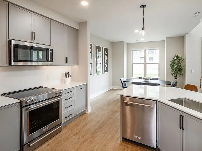 Signature Collection Townhome kitchen with upgraded stainless steel appliances, white quartz countertops and backsplash, grey cabinetry, hard surface flooring, and pendant lighting