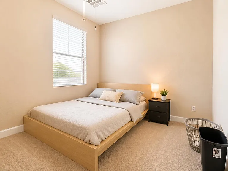 Spacious bedroom with a large window, comfortable bed setup, and a nightstand with lamp for convenient bedside storage.