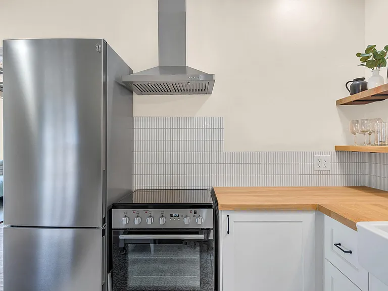 Efficient kitchen with stainless-steel range and refrigerator, vent hood, tiled backsplash, and generous butcher-block counte