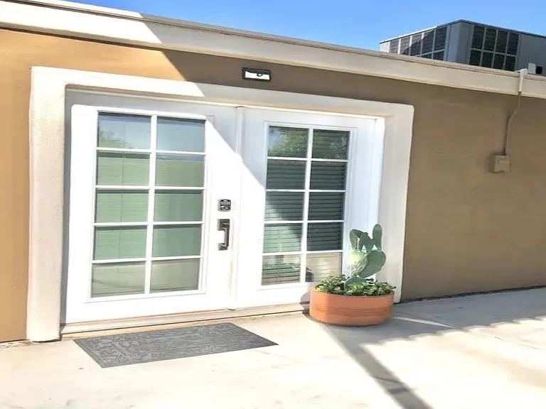 Detached casita entrance at, Tempe rental home. Features bright white French doors with a secure keyless smart lock, a decorative welcome mat, a potted prickly pear cactus, and clean stucco. Perfect private guest setup for a Tempe, AZ stay.