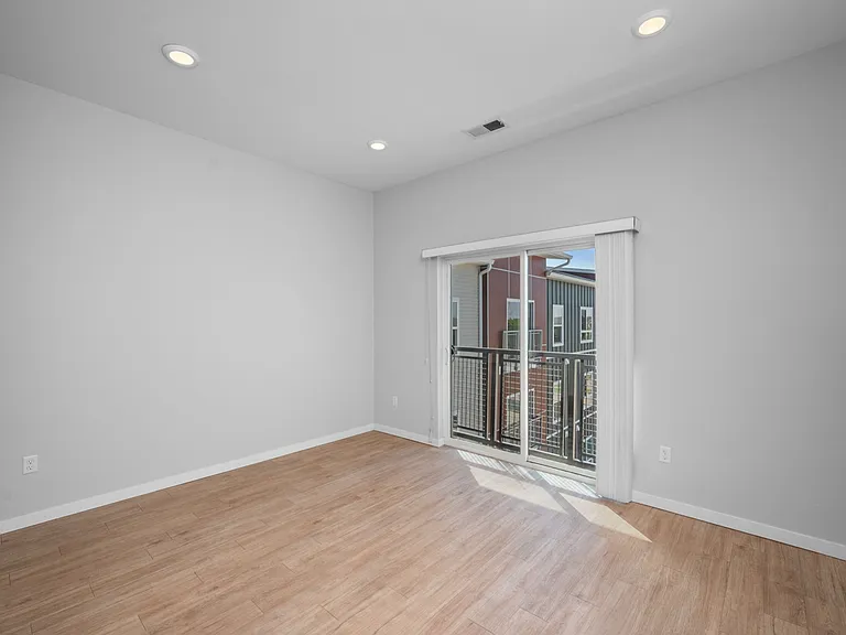 Bright and modern empty room with sleek wooden flooring and large sliding doors opening to a balcony. Bright and modern empty room with sleek wooden flooring and large sliding doors opening to a balcony.