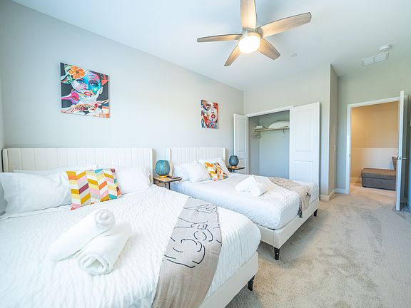 The bedroom displays two beds, stylish decor, and ample natural light, with a fan overhead and a closet in the background, offering a relaxing retreat.
