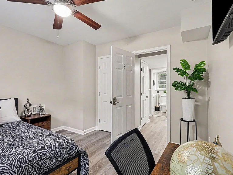 Furnished bedroom with ceiling fan, wood-look flooring, and easy access to the hallway and nearby bath.