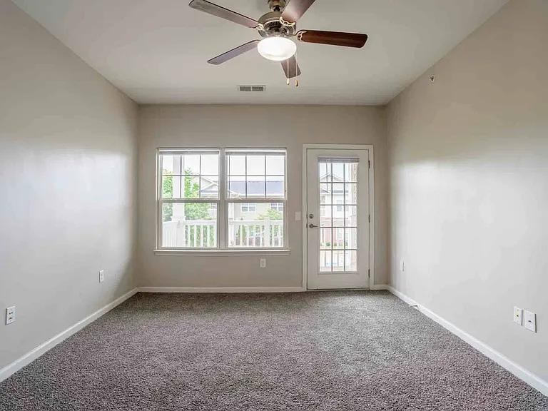 Bright living room with ceiling fan, plush carpet flooring, and direct access to private balcony at Cedar Terrace Apartments.
