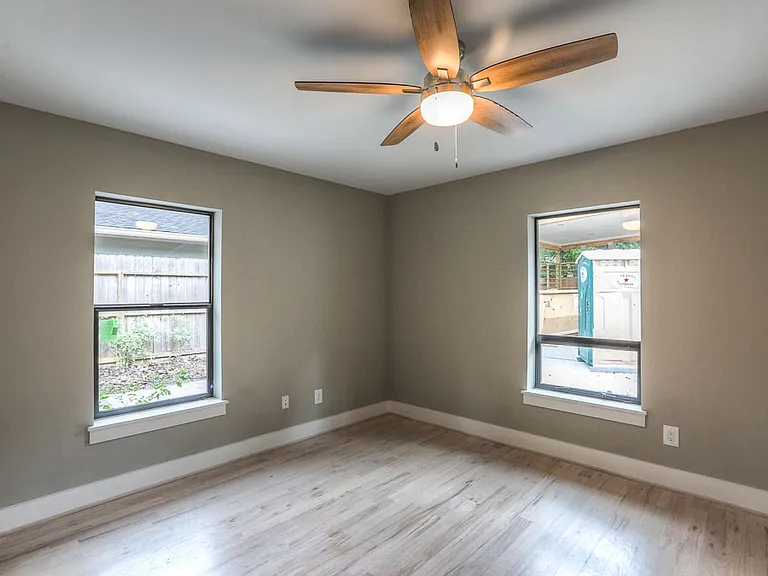 Bright bedroom with tray ceiling, ceiling fan, and two windows looking onto the backyard