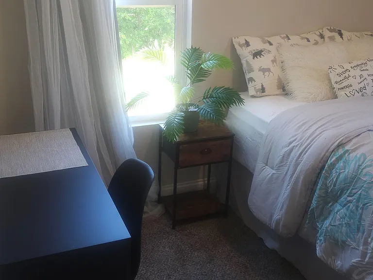 Bedroom with a comfortable bed, side table, and a dedicated desk area, plus a large window with curtains.