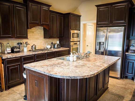 Now THIS is a kitchen! Warm dark brown JKraft cabinets w/raised door panels; huge eat-in island, convenient coffee prep-area, stone back splash, and recessed lighting. Wow!