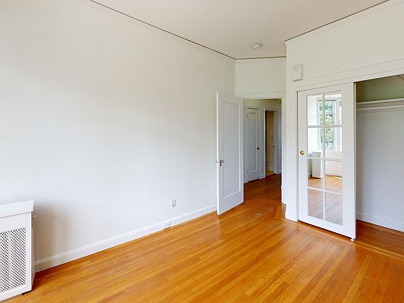 Bright, spacious room with wooden floors, a radiator, and a glass-paneled closet door leading to another room