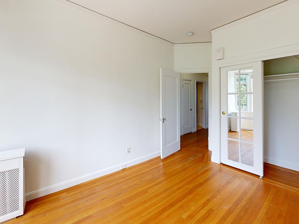 Bright, spacious room with wooden floors, a radiator, and a glass-paneled closet door leading to another room