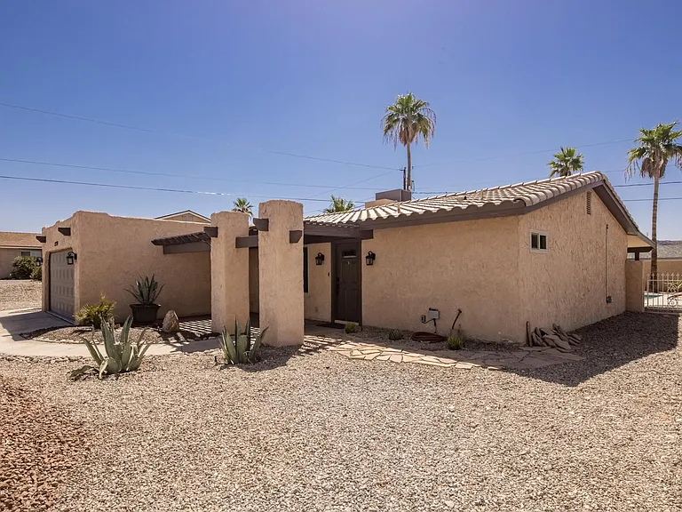Desert-style exterior with stucco finish, covered entry, and mature landscaping.