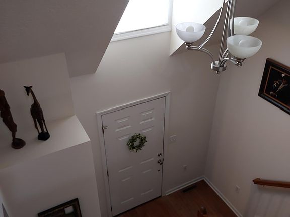 Beautiful vaulted ceiling in the foyer featuring hardwood flooring and an oversized window that fills the entryway with natural light. A decorative hanging fixture adds charm and enhances the open, airy feel of the space.