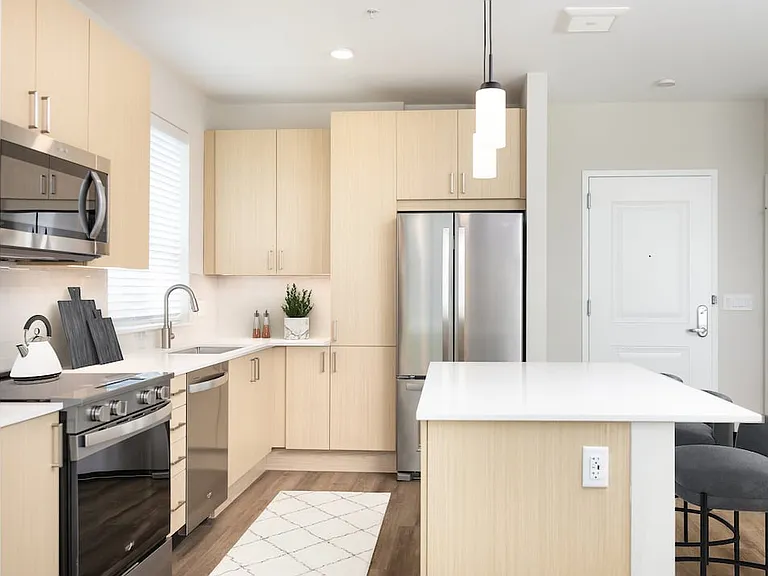Upgrade Collection I kitchen with stainless steel appliances, white quartz countertops, white tile backsplash, light oak cabinetry, and hard surface flooring
