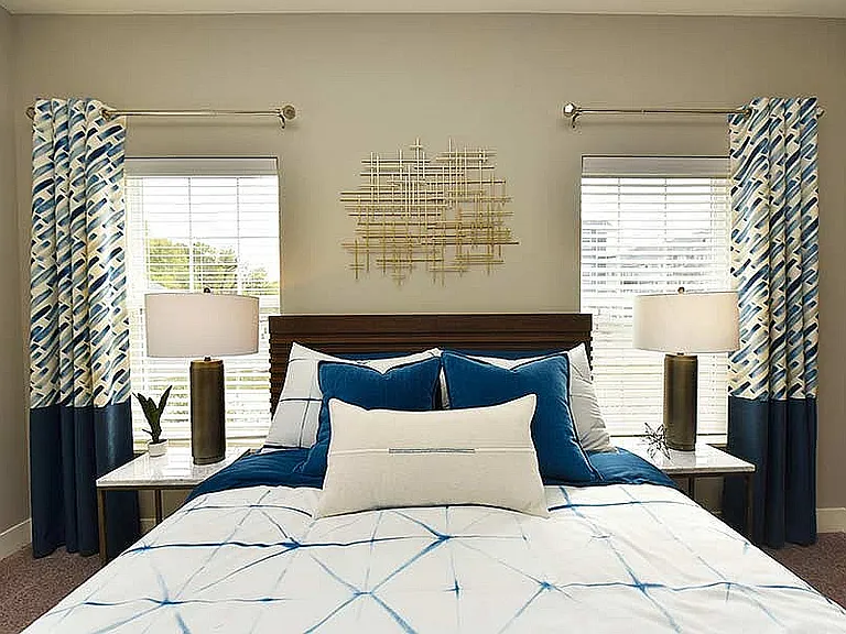 Bright and breezy, this bedroom offers symmetry, sunshine, and serene style_perfectly framed between two large windows.