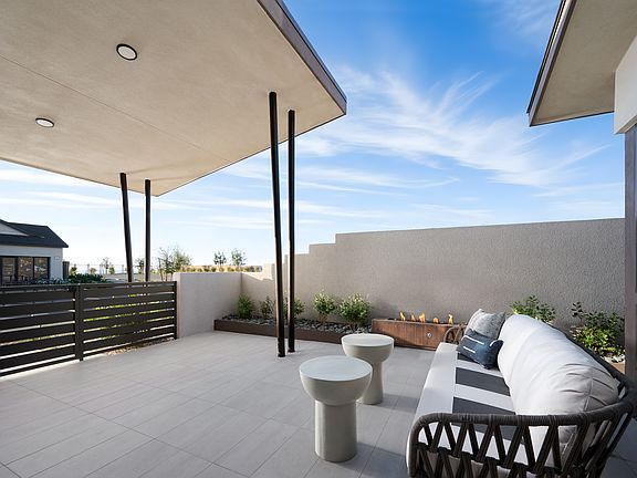 A modern outdoor patio with a covered seating area, surrounded by a low fence and featuring a clear