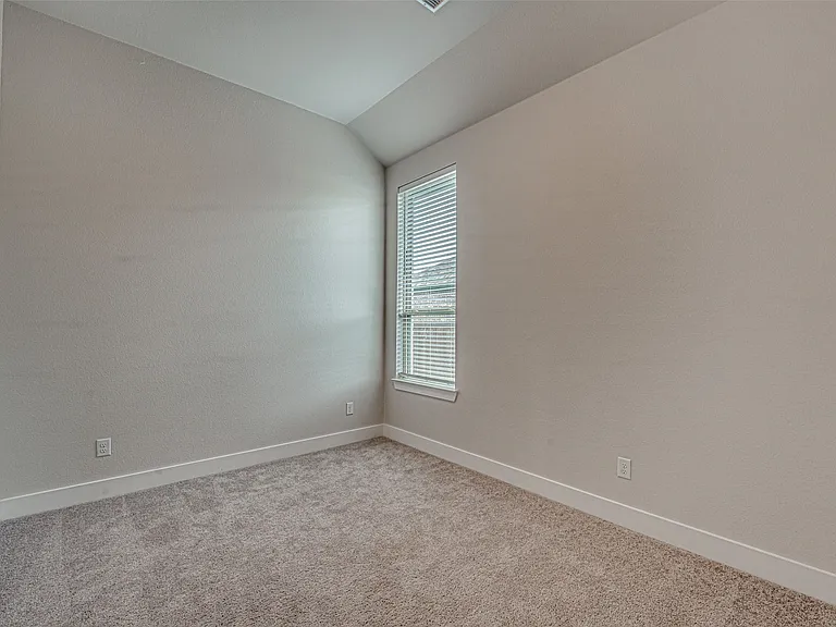 Spacious room featuring vaulted ceilings, neutral-toned walls, and plush carpet flooring