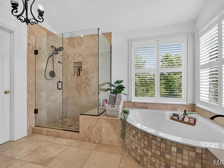 Spacious bathroom featuring a built-in soaking tub with mosaic tile surround, an enclosed glass shower with tiled walls and a built-in niche, and large windows with plantation shutters