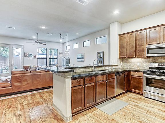 Open kitchen has rich custom wood cabinets, granite counters, and natural stone backsplash.