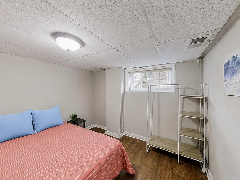 Private bedroom with a full bed, wood-look flooring, overhead lighting, and a window plus open shelving for storage.