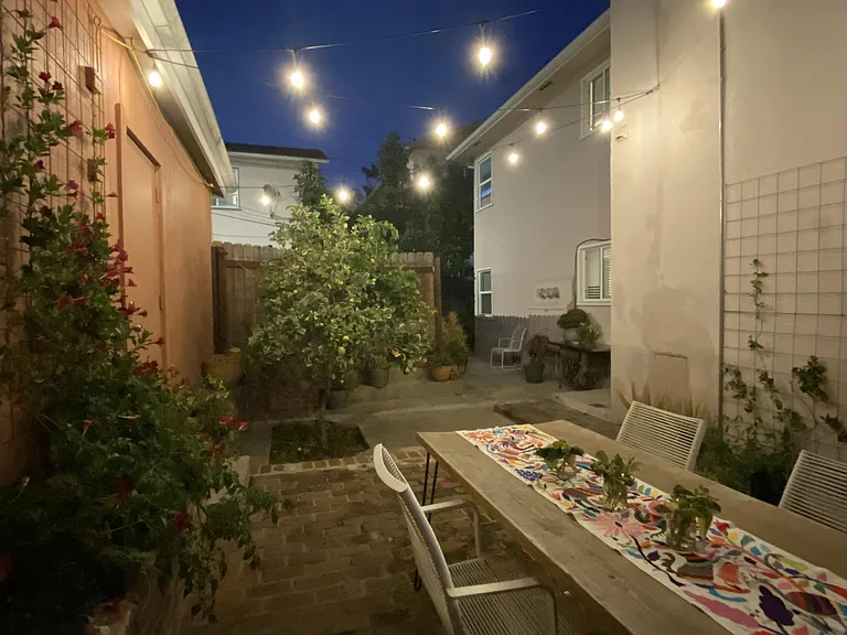 Patio with huge shade canopy, edison string lights, an exterior power plug so you can sit outside and work on your computer, tons of plants, and a pink lemonade lemon tree! Night shot.
