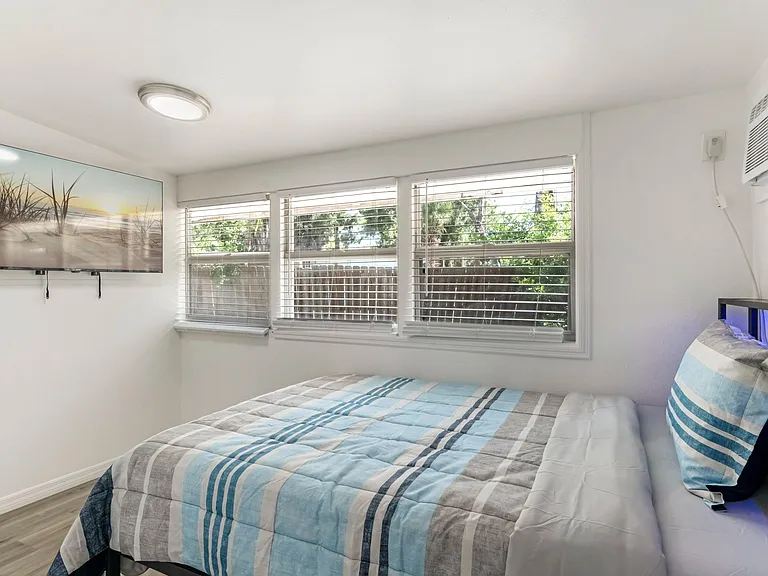 Private bedroom with large windows, blinds, and a comfortable bed setup with easy access to in-room AC.