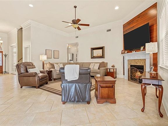Living room with a fireplace, crown molding, light tile patterned flooring, and ceiling fan with notable chandelier