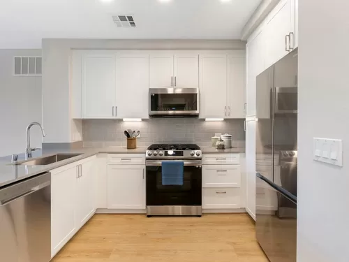 Renovated Package I kitchen with stainless steel appliances, grey quartz countertops, white cabinetry, grey tile backsplash, and hard surface flooring - Avalon Encino