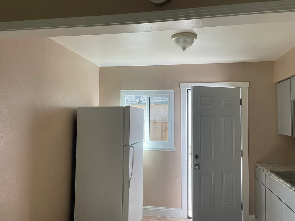Refrigerator and kitchen with entrance to enclosed backyard.
