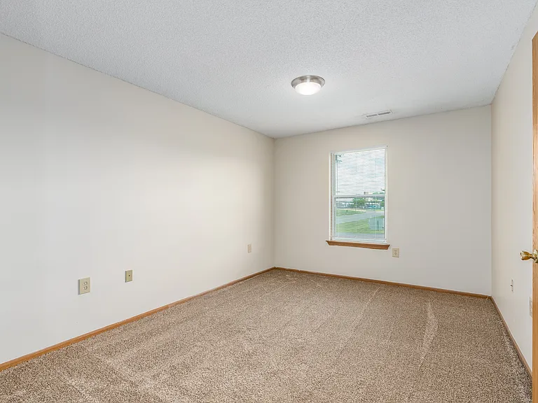 Carpeted bedroom and window with blinds of River Valley apartment home in Lancaster, OH.
