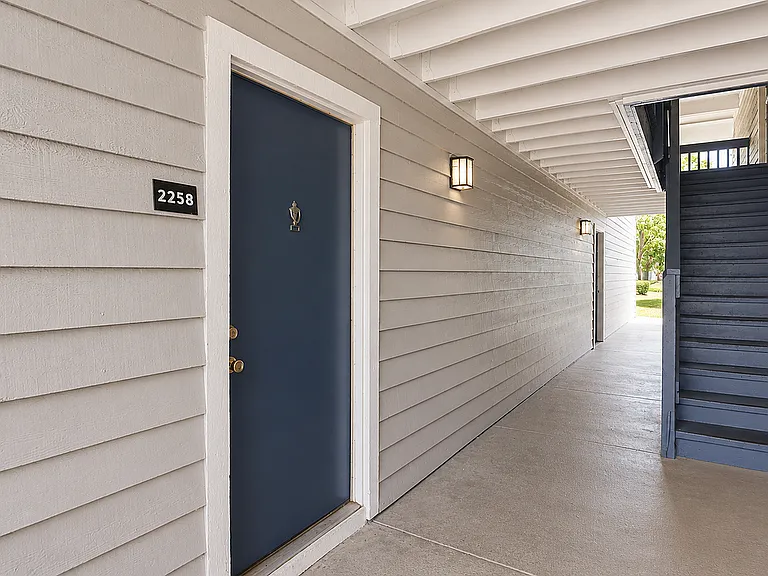 Inviting apartment entrance with elegant blue door and neatly painted siding, complemented by ambient lighting and a nearby staircase offering easy access.